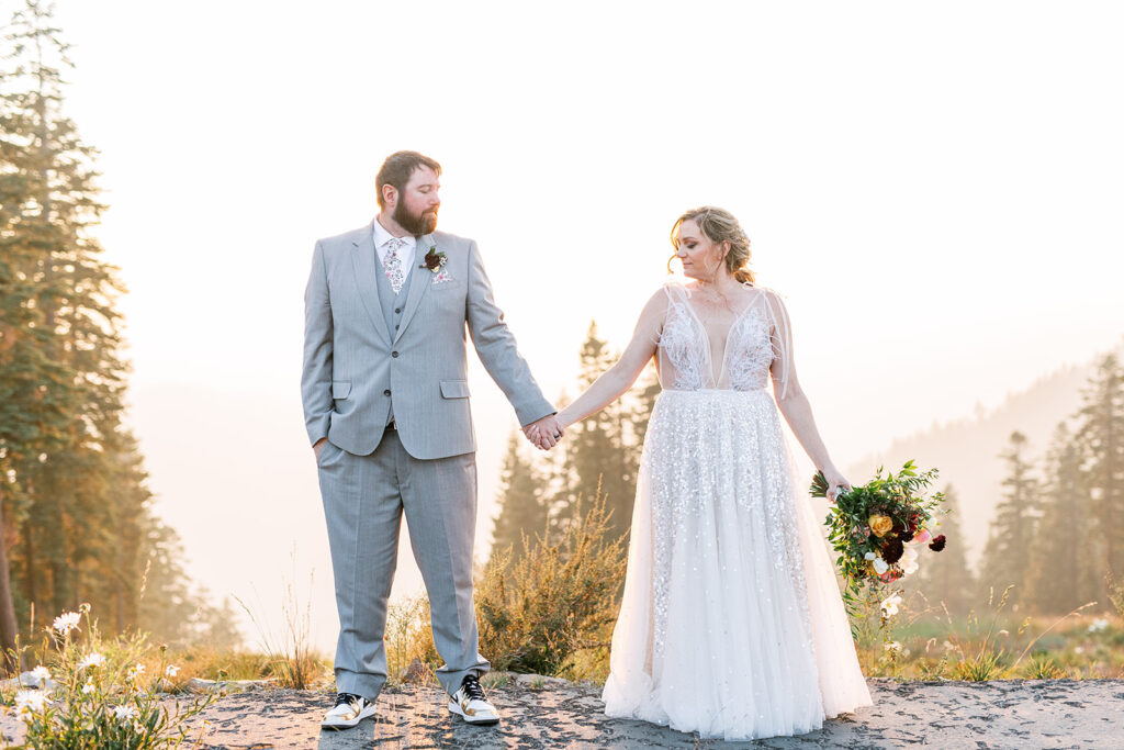 Bride and groom stand on top of a mountain with the sunset behind them